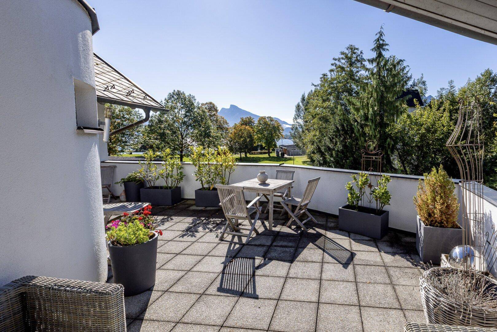 Große, geflieste Terrasse mit Pflanzenkübeln, Sitzgelegenheiten und Bergblick.