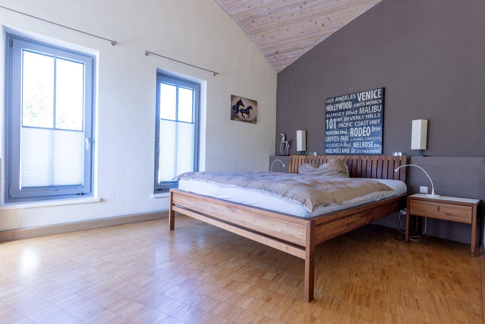 Modernes Schlafzimmer mit Holzbett, Parkettboden und schräger Decke.