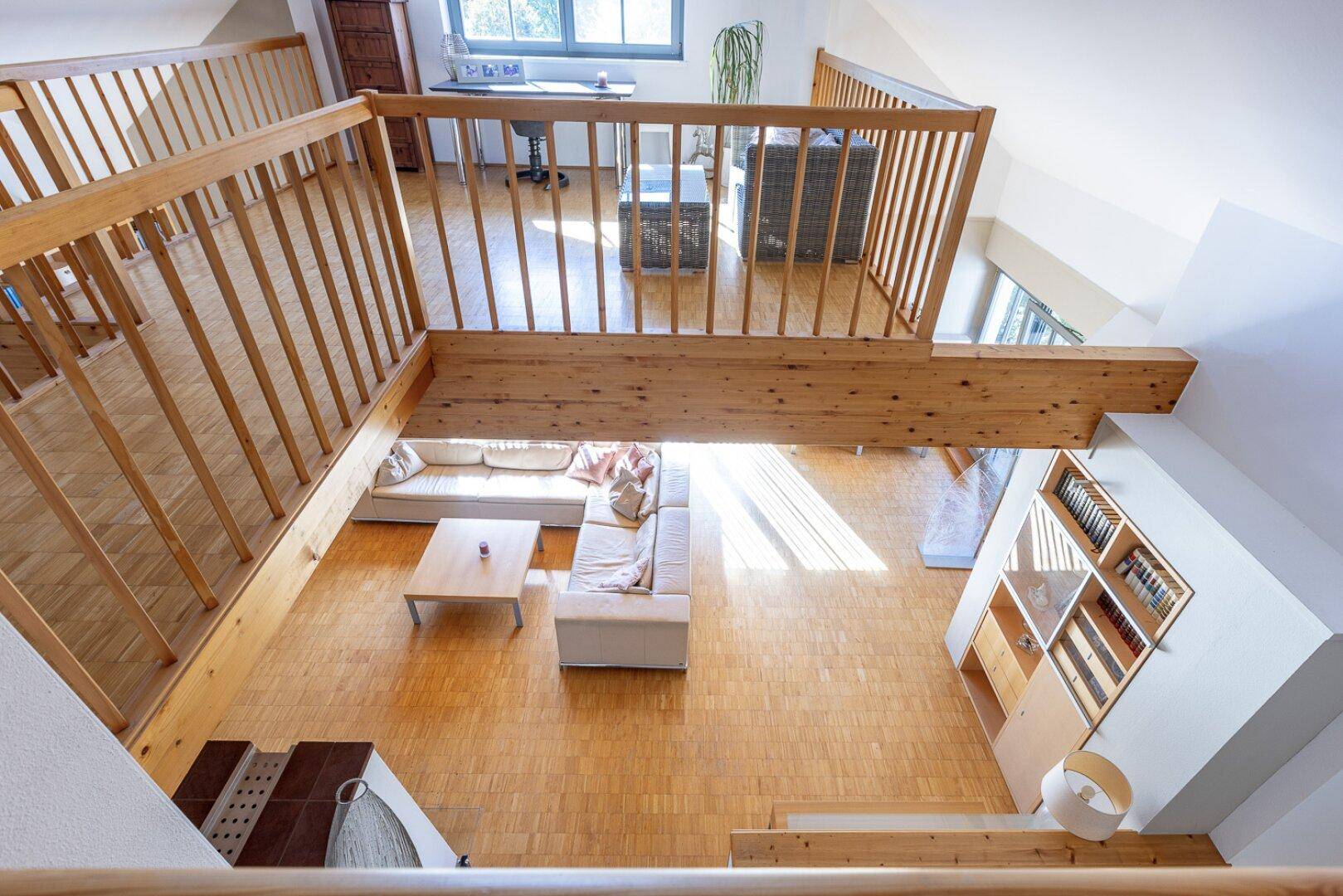 Blick von der Galerie auf das geräumige Wohnzimmer mit Parkettboden und großer Couch.