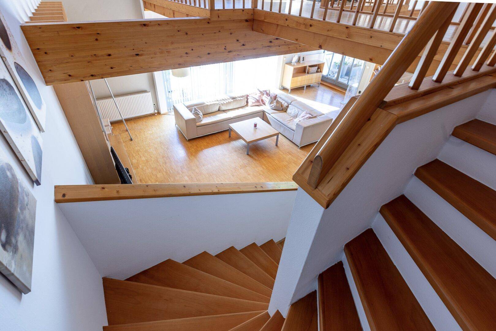 Blick von der Holztreppe in ein helles Wohnzimmer mit Holzbalken und gemütlicher Sitzecke.