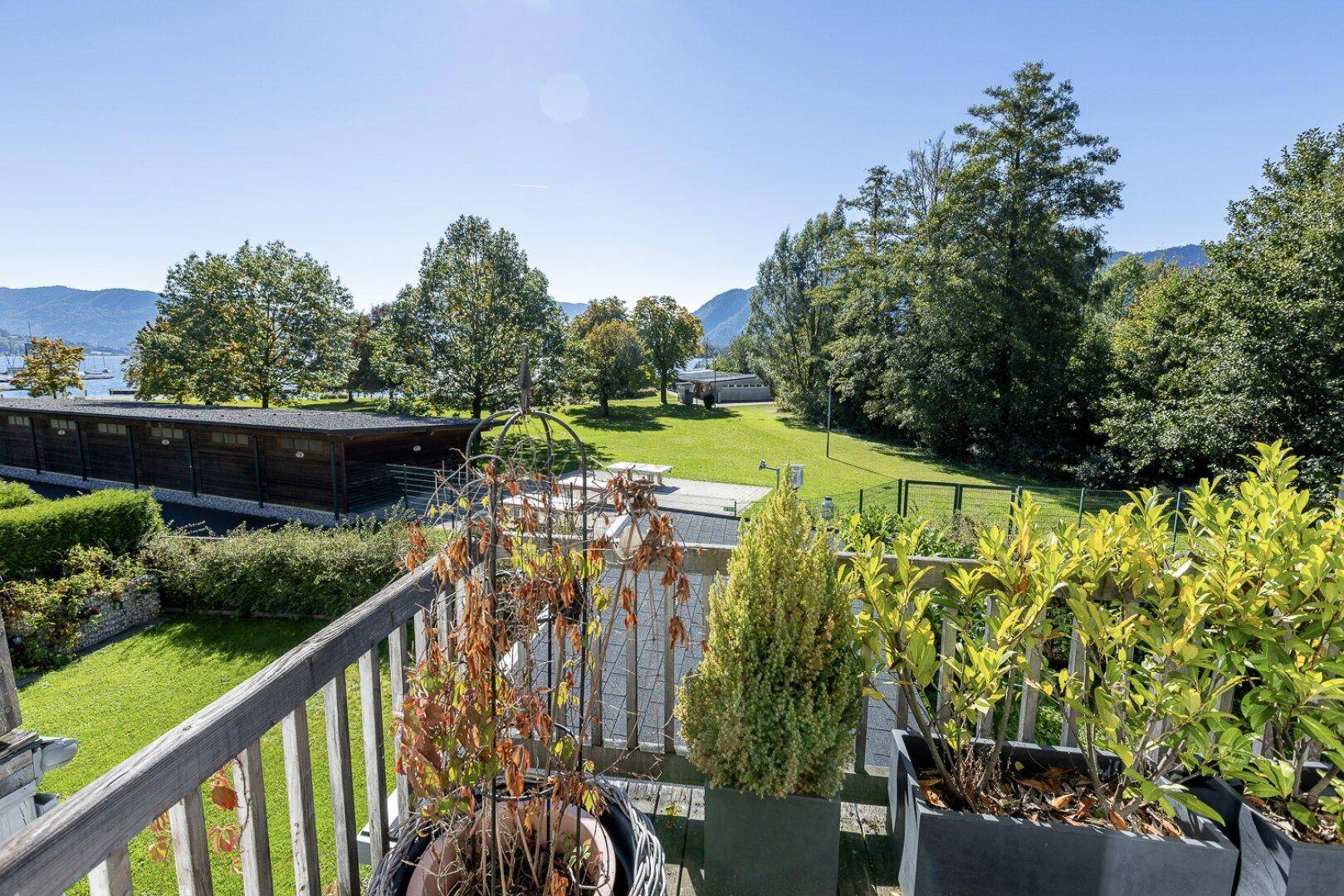 Sonniger Balkon mit Pflanzen und weitem Blick auf den See und die umliegenden Berge.