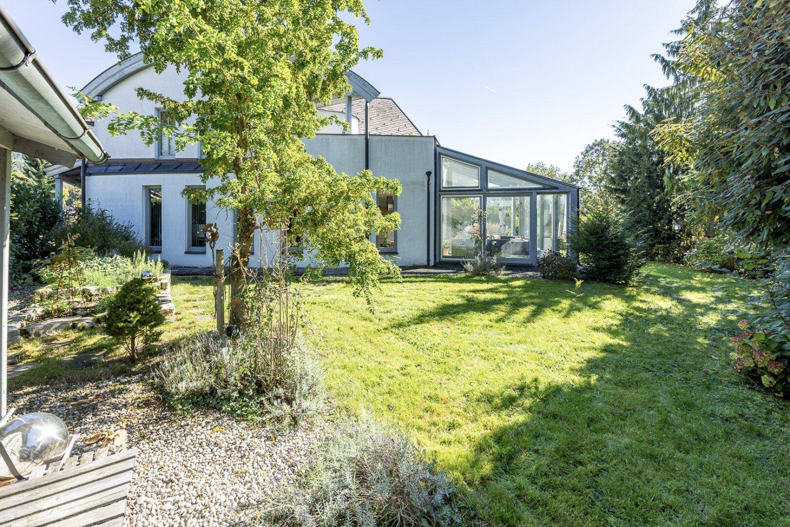Weitläufiger Garten mit Rasenfläche, Bäumen und einem modernen Wintergarten am Haus.