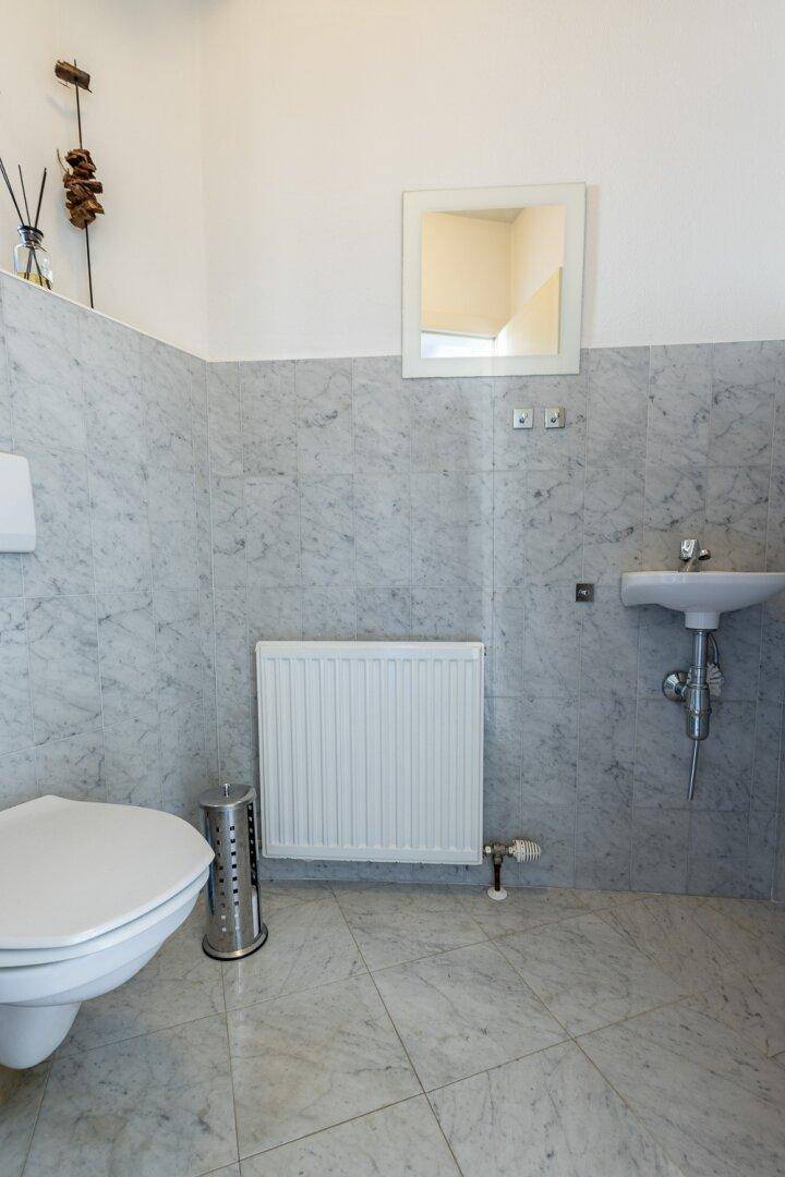 Helles Gäste-WC mit hellgrauen Marmorfliesen, Toilette und kleinem Waschbecken.