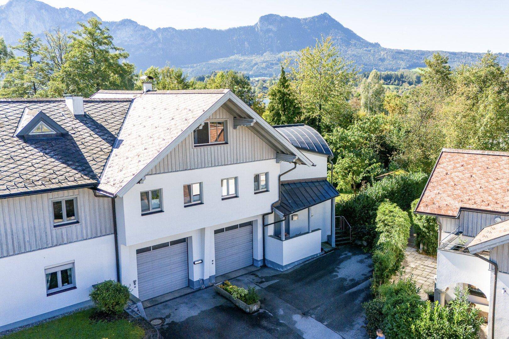 Luftaufnahme des Hauses mit Garagen, Garten und beeindruckendem Bergblick im Hintergrund.