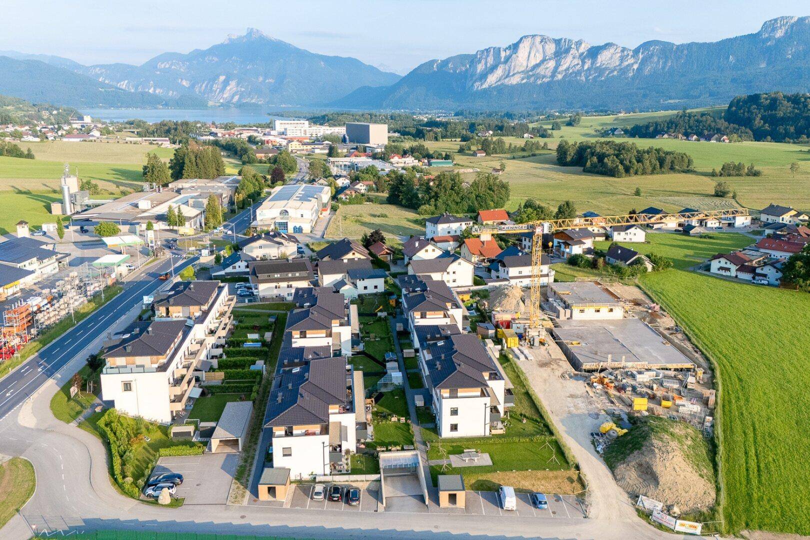 Luftaufnahme einer modernen Wohnsiedlung im Bau mit Blick auf Berge und See.