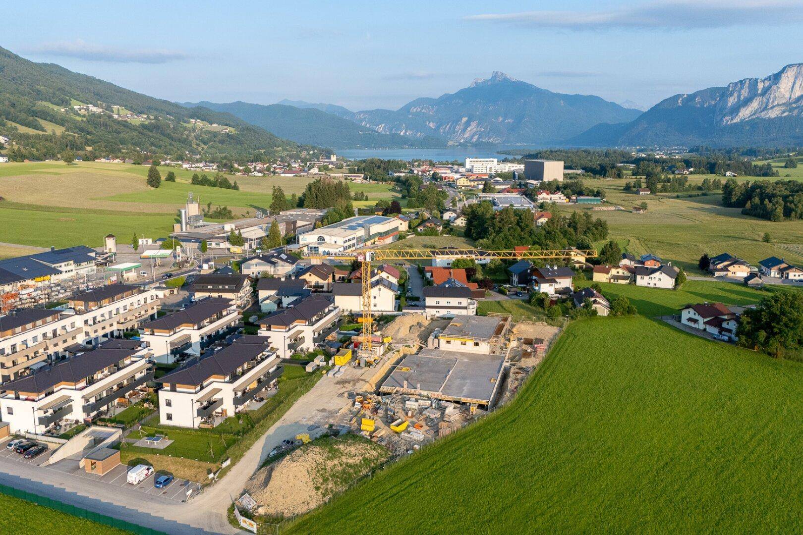 Luftaufnahme einer neuen Wohnsiedlung im Bau mit See- und Bergblick in ländlicher Umgebung.