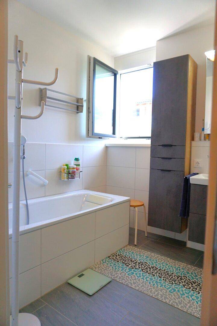 Modernes Badezimmer mit Badewanne, Fenster und grauen Bodenfliesen sowie einem farbigen Teppich.