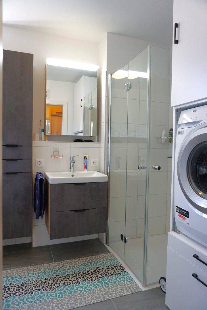 Badezimmer mit integrierter Waschmaschine und Trockner in einem praktischen Hochschrank neben der Dusche.