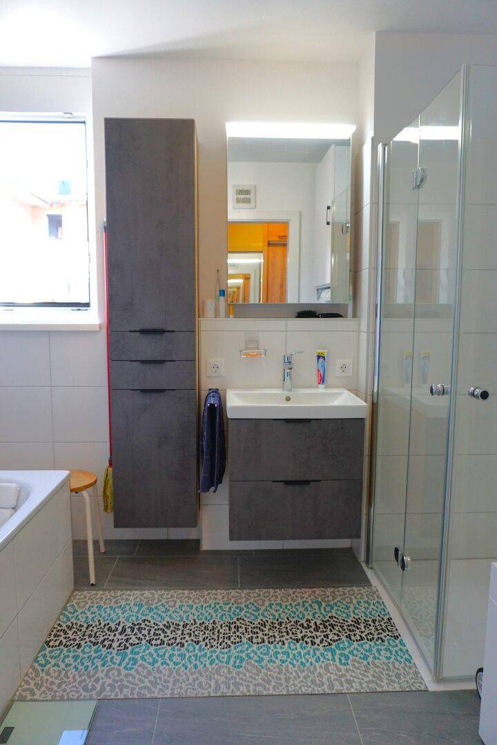 Helles Badezimmer mit Waschtisch, Spiegelschrank und einer Duschkabine mit Glaswänden.