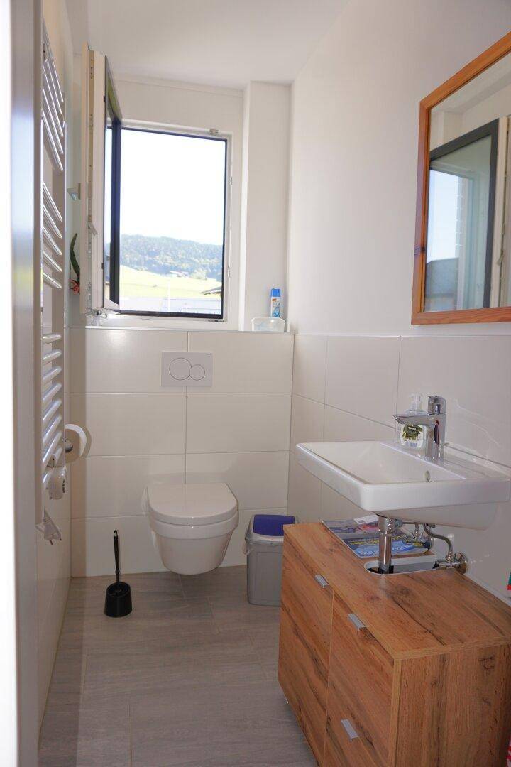 Separates WC mit wandhängender Toilette, Waschbecken, Fenster und beheiztem Handtuchhalter.