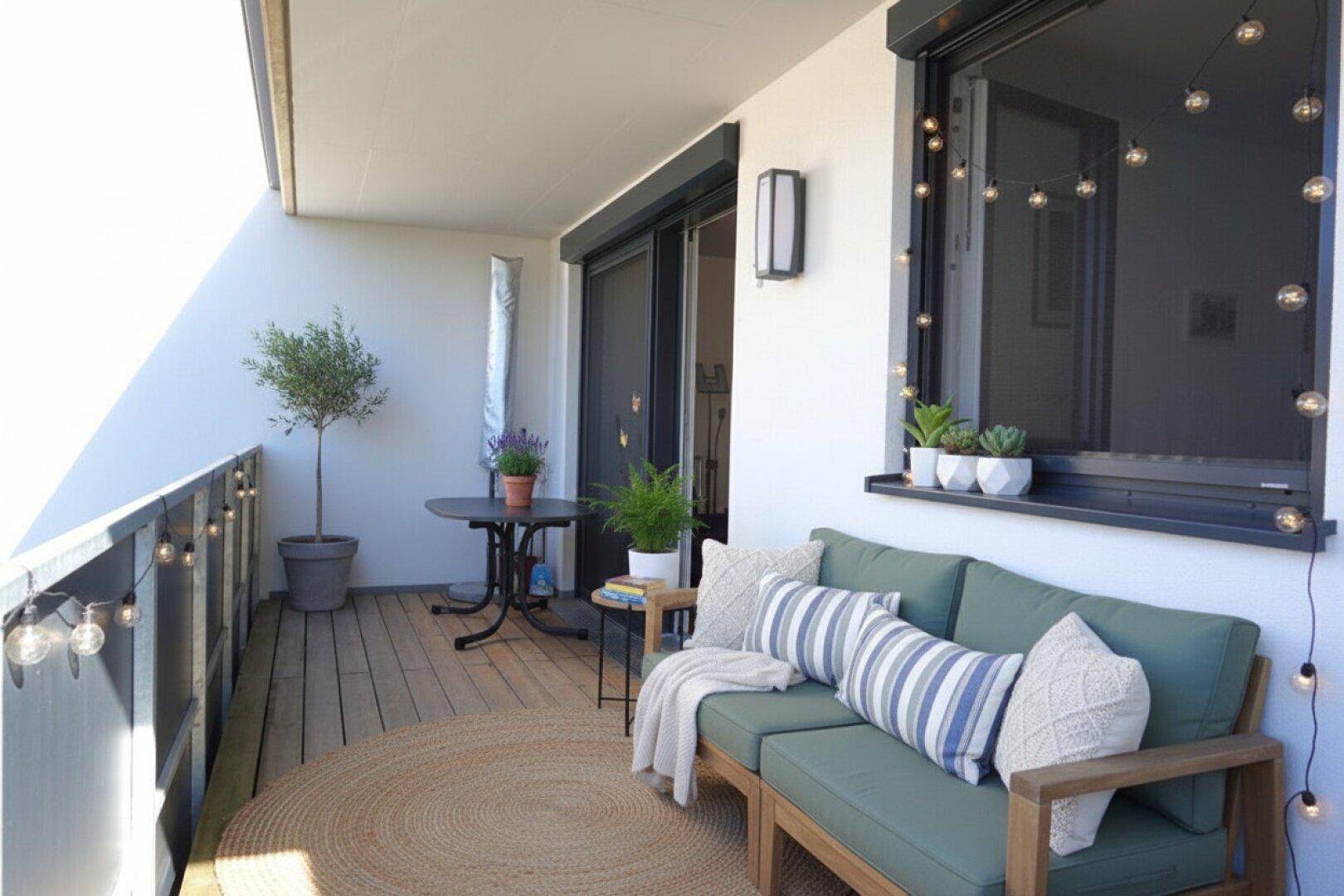 Gemütlicher Balkon mit Holzboden, bequemer Sitzgelegenheit und dekorativer Lichterkette.