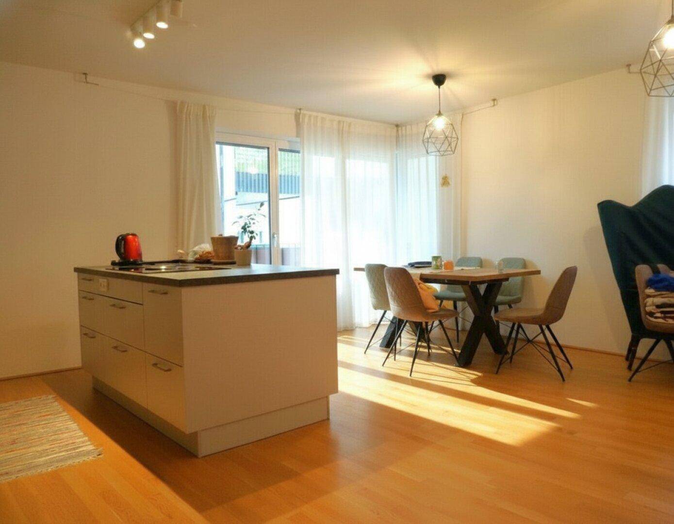 Offener Wohn- und Essbereich mit Kücheninsel, Esstisch und Zugang zum sonnigen Balkon.