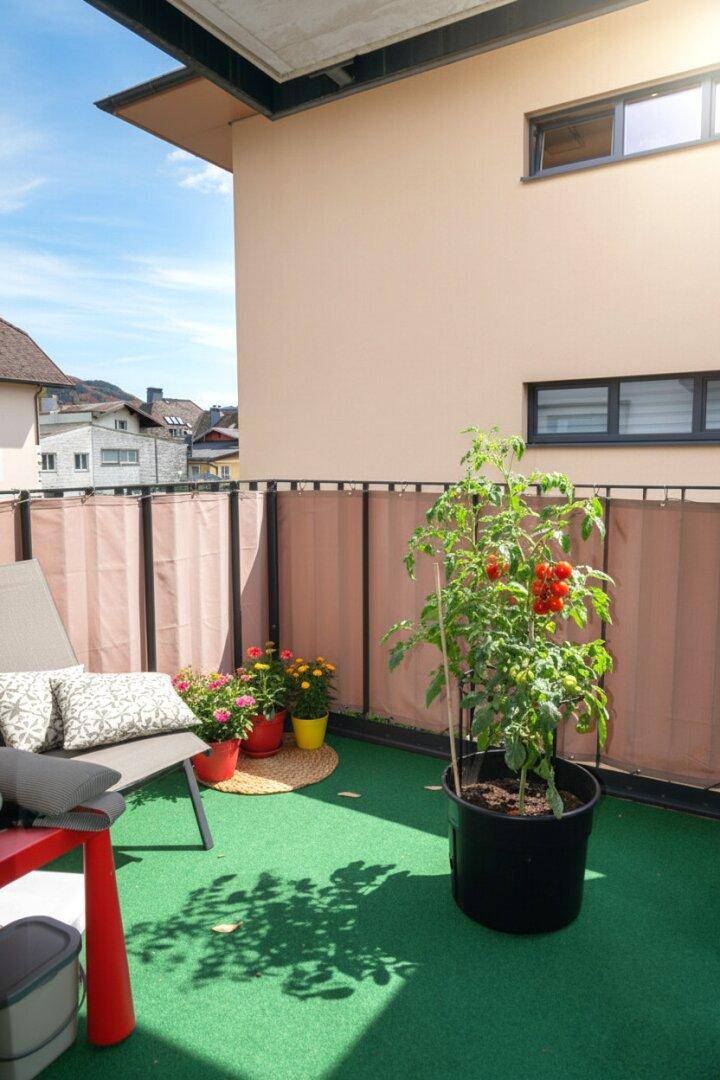Sonniger Balkon mit Kunstrasen, Tomatenpflanze und gemütlicher Sitzgelegenheit im Freien.