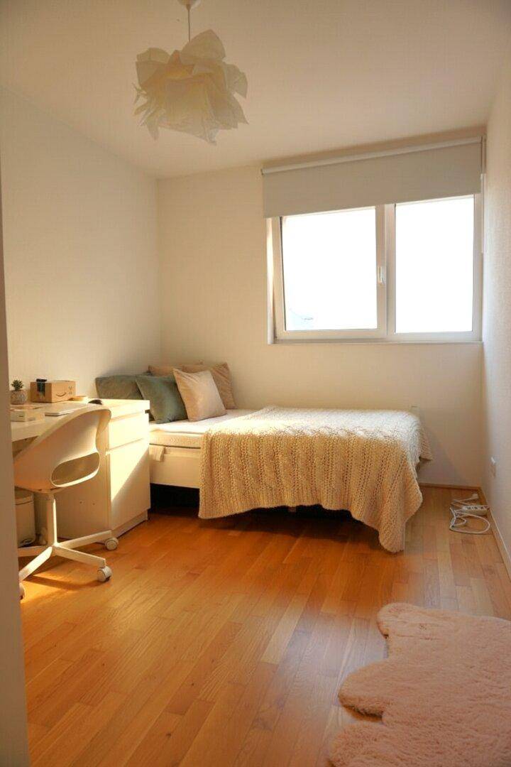 Gemütliches Schlafzimmer mit Einzelbett, Schreibtisch und hellem Parkettboden, gut beleuchtet.