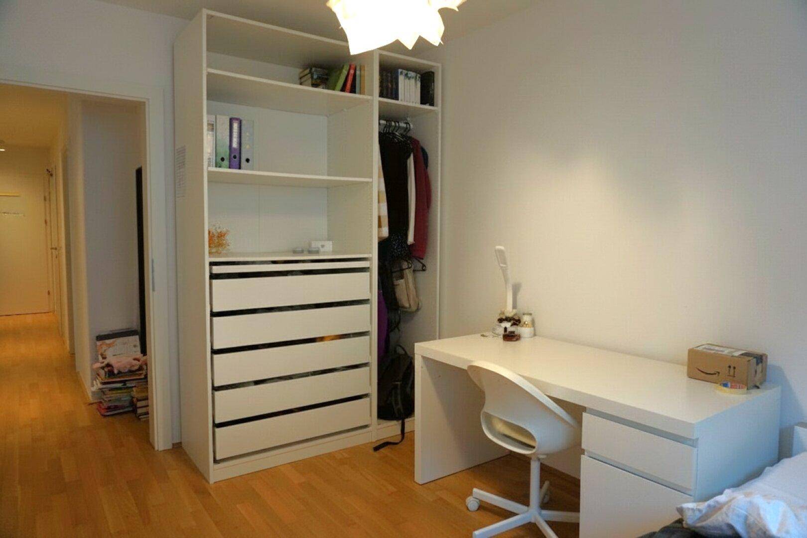 Schlafzimmer mit praktischem Einbauschrank, Schreibtisch und hellem Parkettboden, funktional eingerichtet.