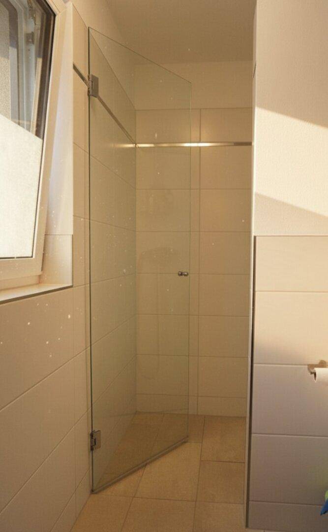 Helle begehbare Dusche mit Glasabtrennung und Fenster, modern gefliest.