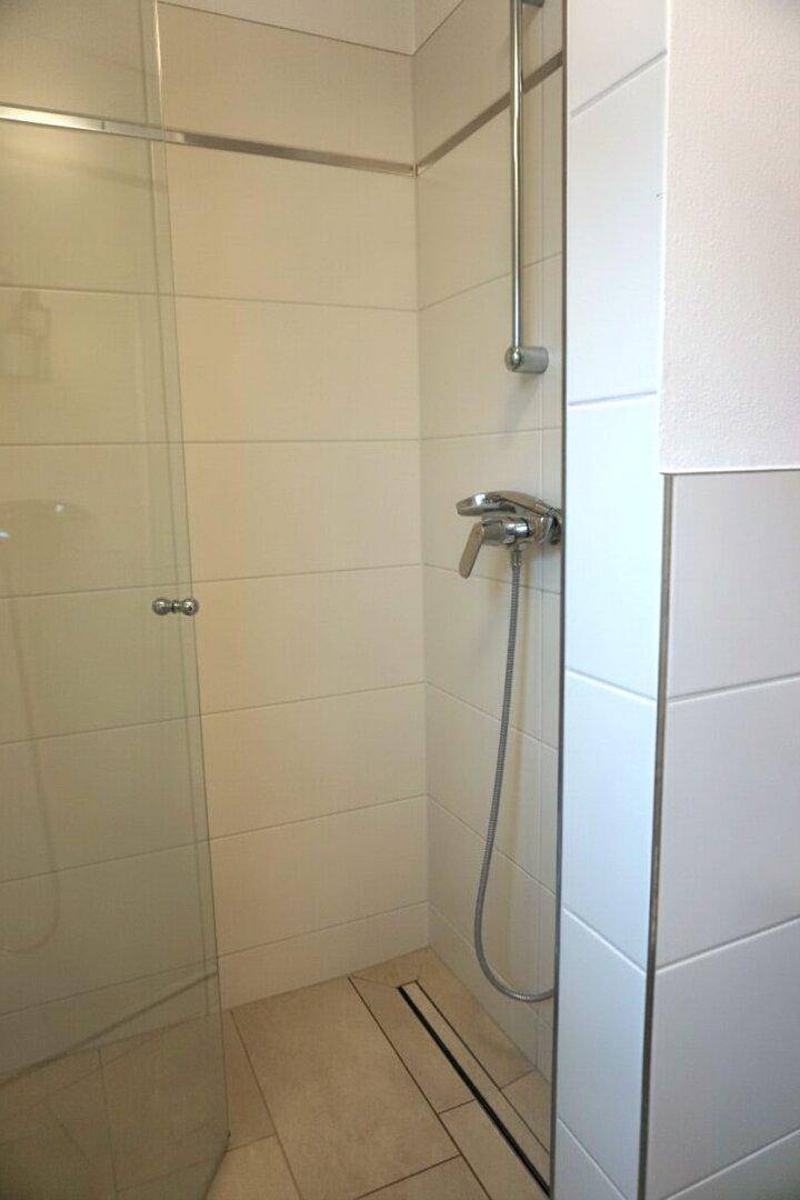 Duschbereich mit moderner Armatur und gefliestem Boden, ausgestattet mit einer Ablaufrinne.