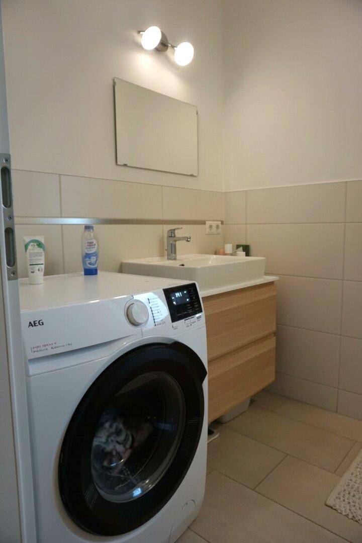 Modernes Badezimmer mit Waschmaschine, Einzelwaschbecken und Holzunterschrank, hell gefliest.