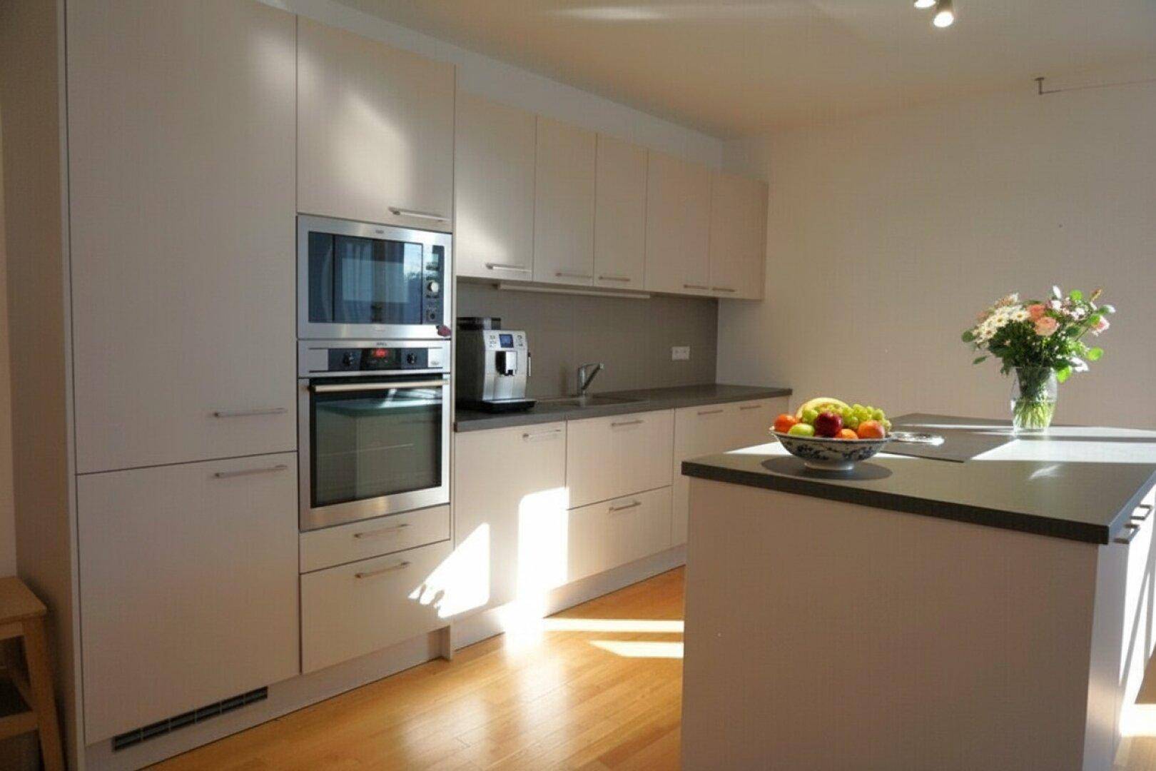 Helle, moderne Küche mit integriertem Backofen und Mikrowelle, sowie einer Kücheninsel.