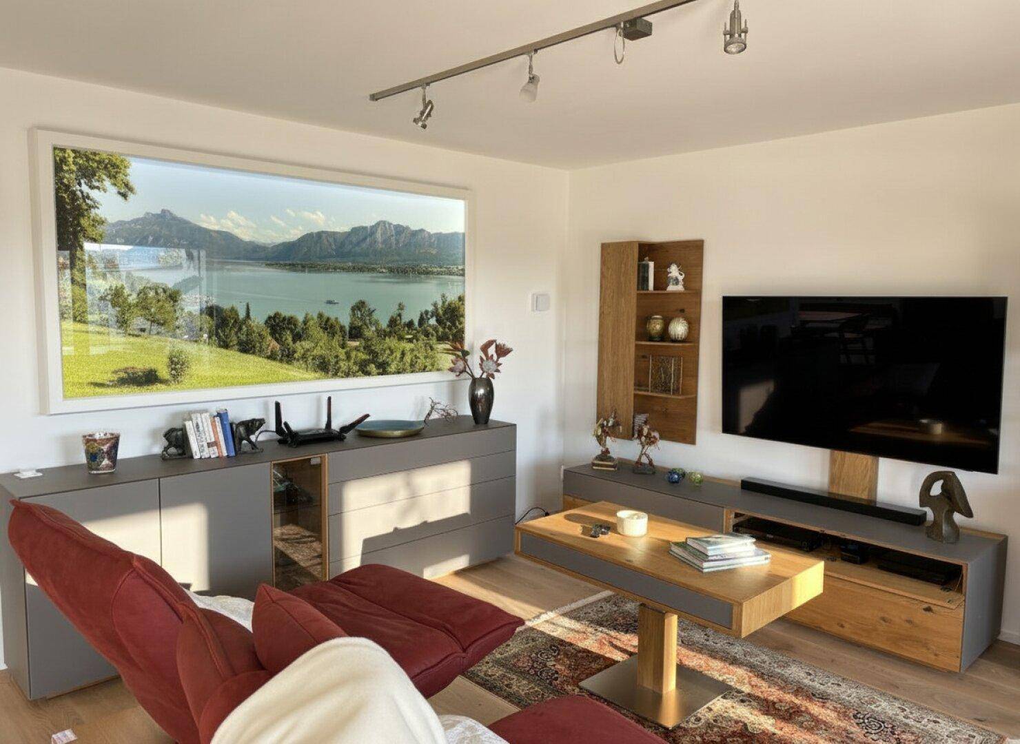 Gemütliches Wohnzimmer mit modernem Mobiliar, Holzboden und einem großen Wandbild mit Seeblick.