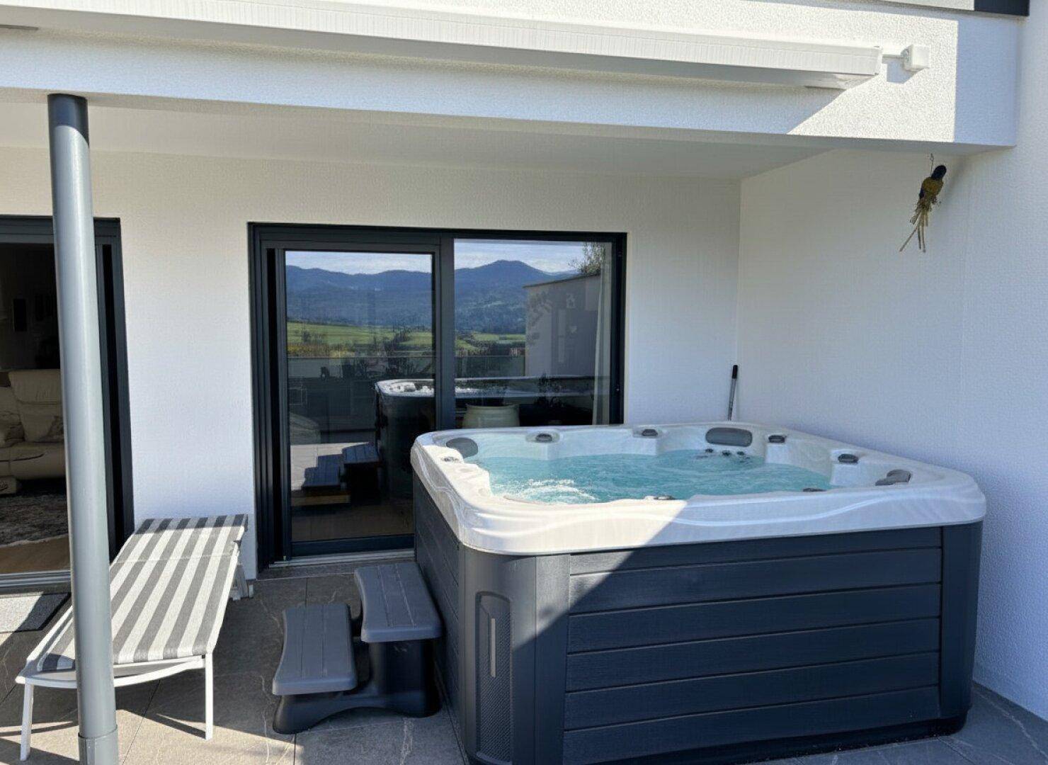 Große Terrasse mit Whirlpool und Liegestuhl, ideal zum Entspannen mit Bergblick.