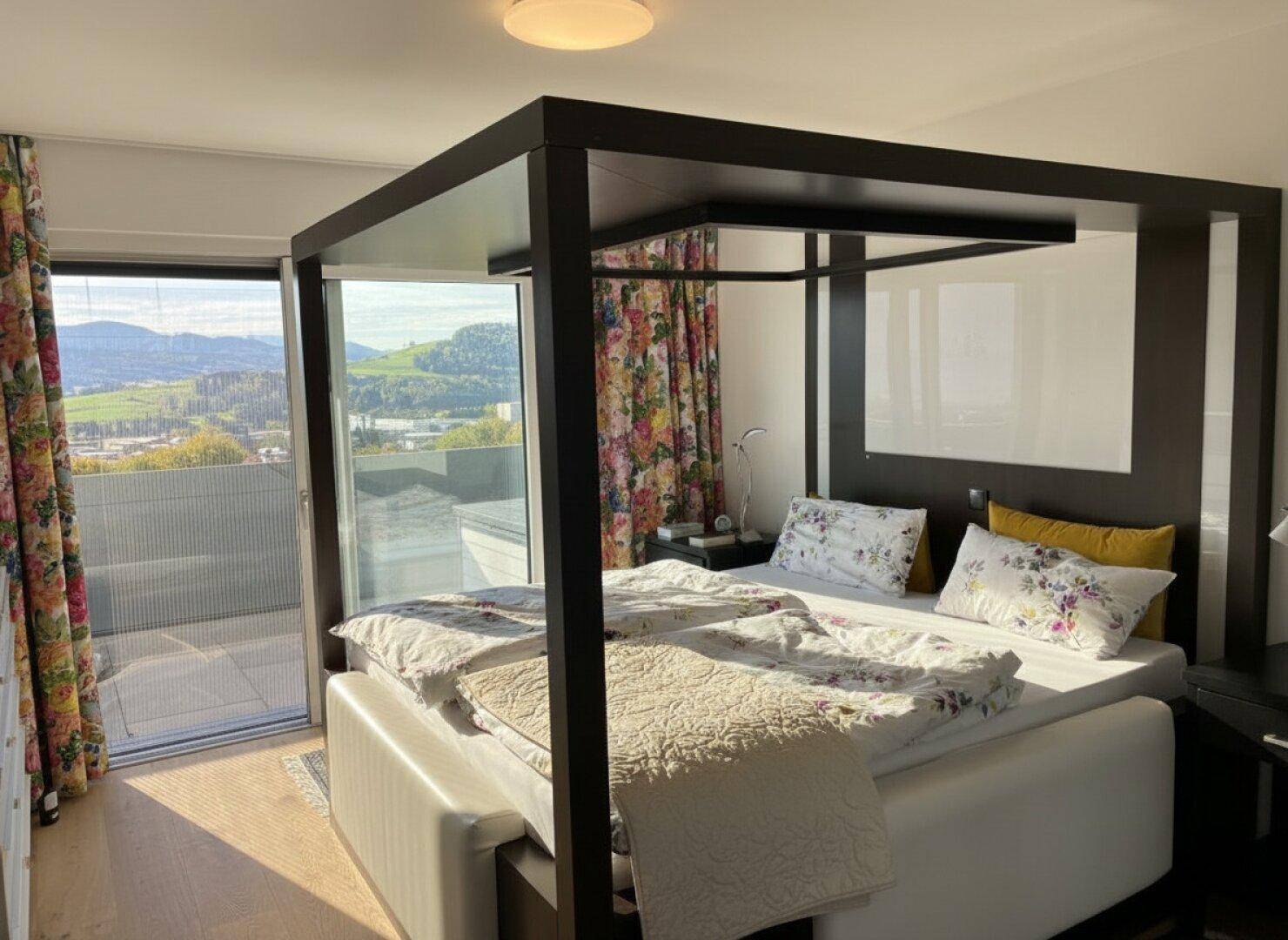 Helles Schlafzimmer mit Himmelbett, farbenfrohen Vorhängen und Zugang zum Balkon mit Weitblick.
