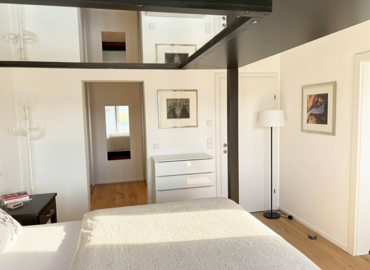 Geräumiges Schlafzimmer mit Holzboden, weißer Kommode und minimalistischer Einrichtung.