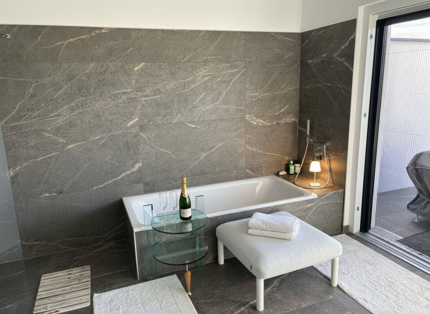 Elegantes Badezimmer mit Badewanne, großformatigen Fliesen und direktem Zugang zur Terrasse.