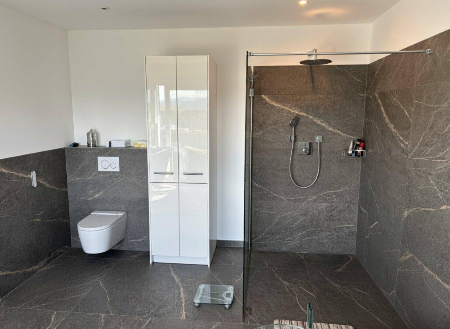 Geräumiges Badezimmer mit bodengleicher Dusche, wandhängendem WC und eleganten Fliesen.