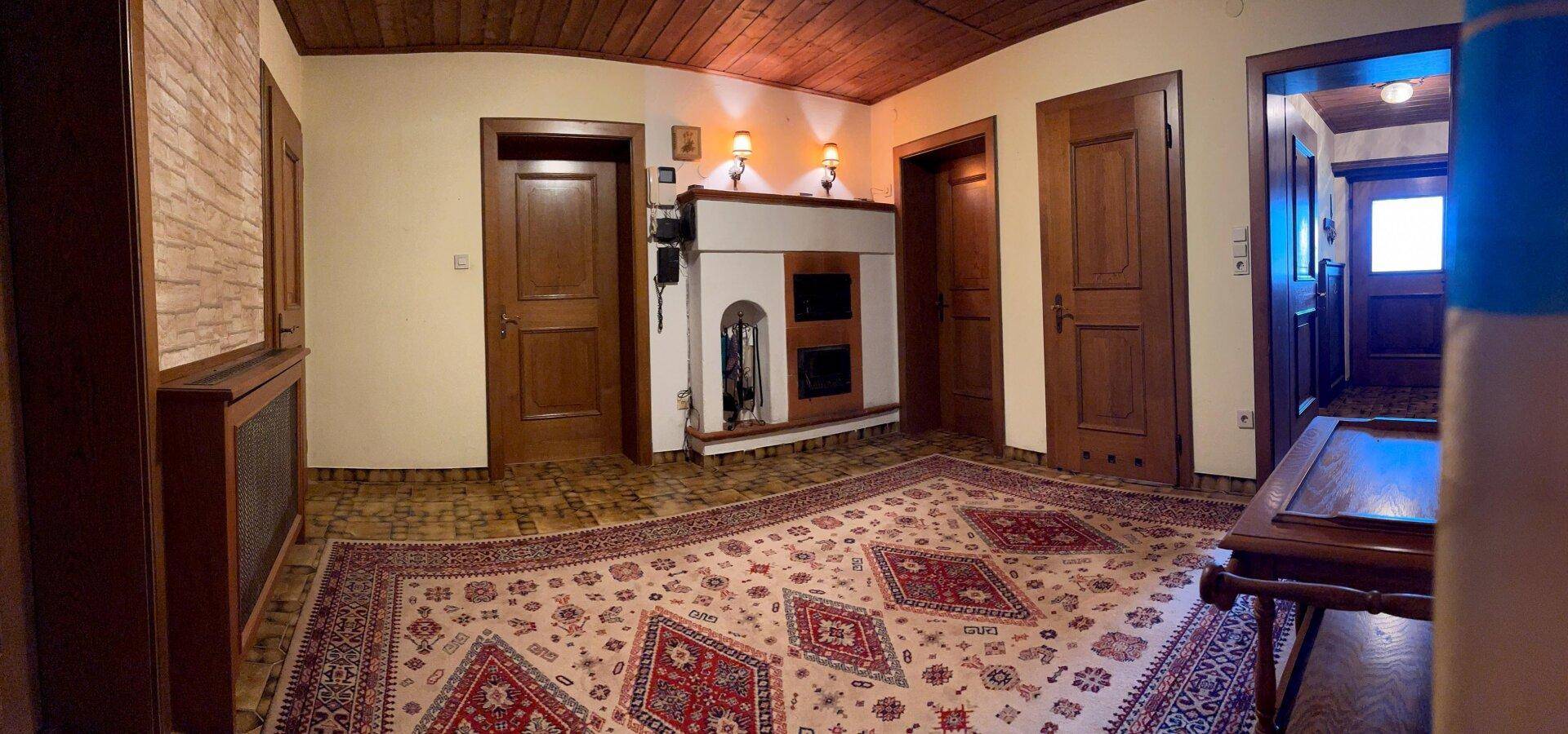 Geräumiger Flur mit traditionellem Kachelofen, Holztüren und gemustertem Teppichboden.