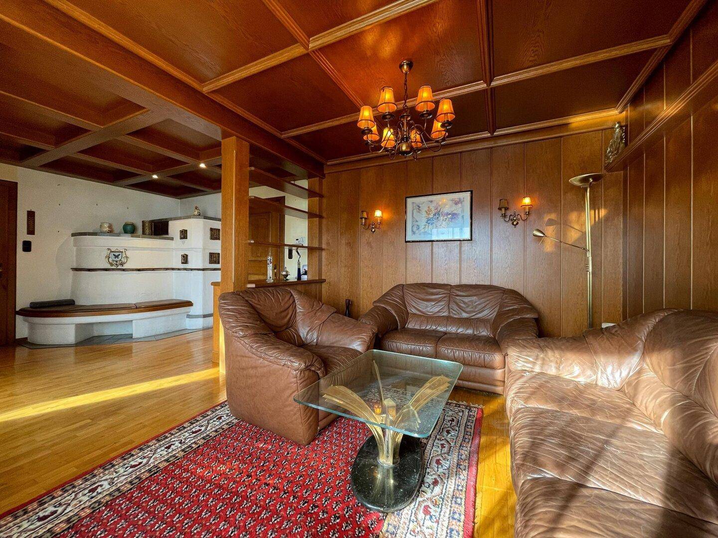 Wohnzimmer mit Ledersitzgruppe, Holzboden und Blick auf den traditionellen Kachelofen.