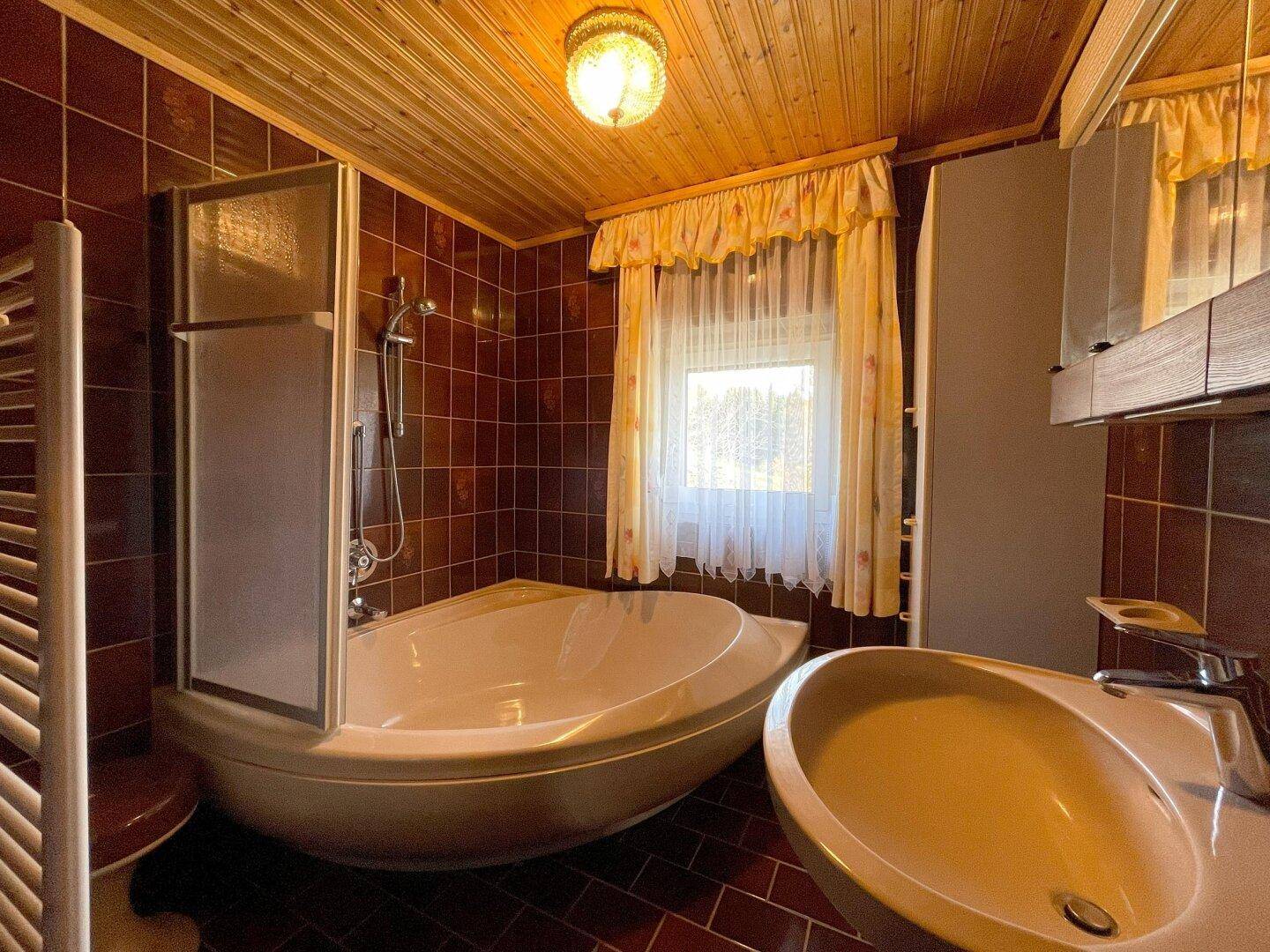 Traditionelles Badezimmer mit braunen Fliesen, Badewanne mit Duschabtrennung und Holzdecke.