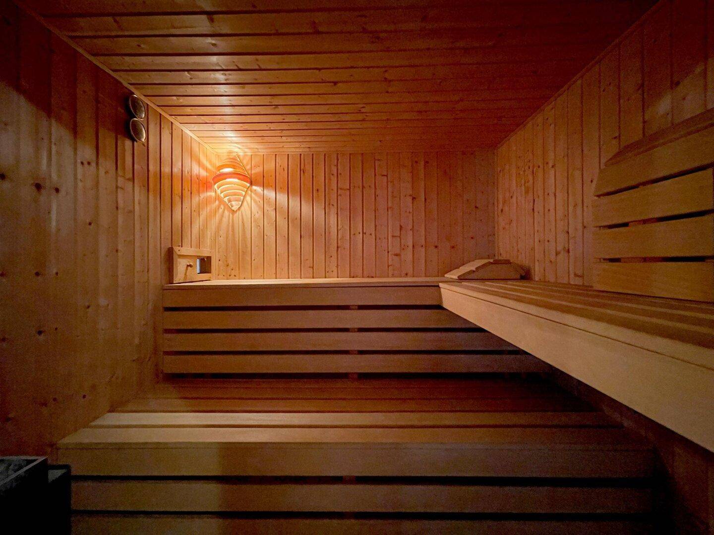 Innenansicht der Sauna mit Holzverkleidung, mehrstufigen Bänken und stimmungsvoller Beleuchtung.
