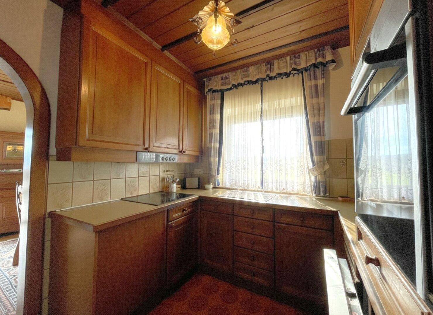 Traditionelle Holzküche mit Einbauschränken, Fliesenrückwand und Blick ins Grüne.