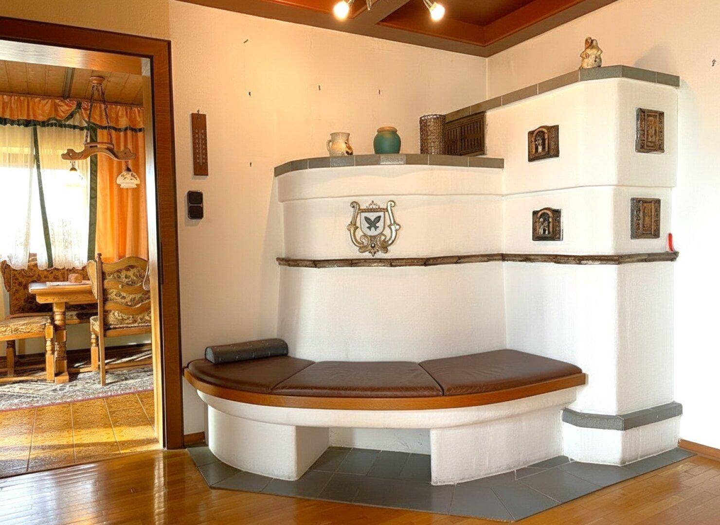Traditioneller Kachelofen mit integrierter Sitzbank, umgeben von Holzböden und einer Holztür.