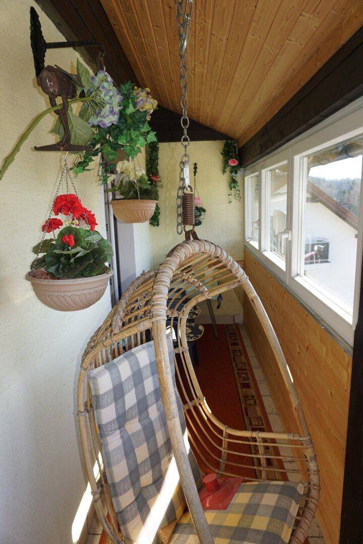 Gemütlicher, verglaster Balkon mit Hängesessel und Holzverkleidung, ideal zum Entspannen.