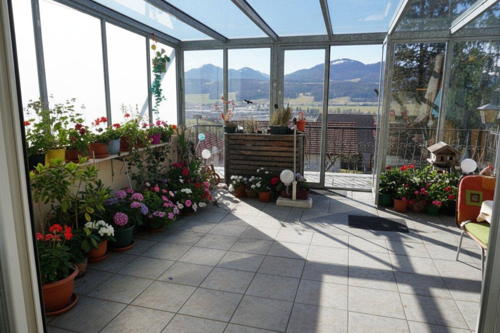 Heller Wintergarten mit vielen Pflanzen, Fliesenboden und weitem Blick auf die Landschaft.