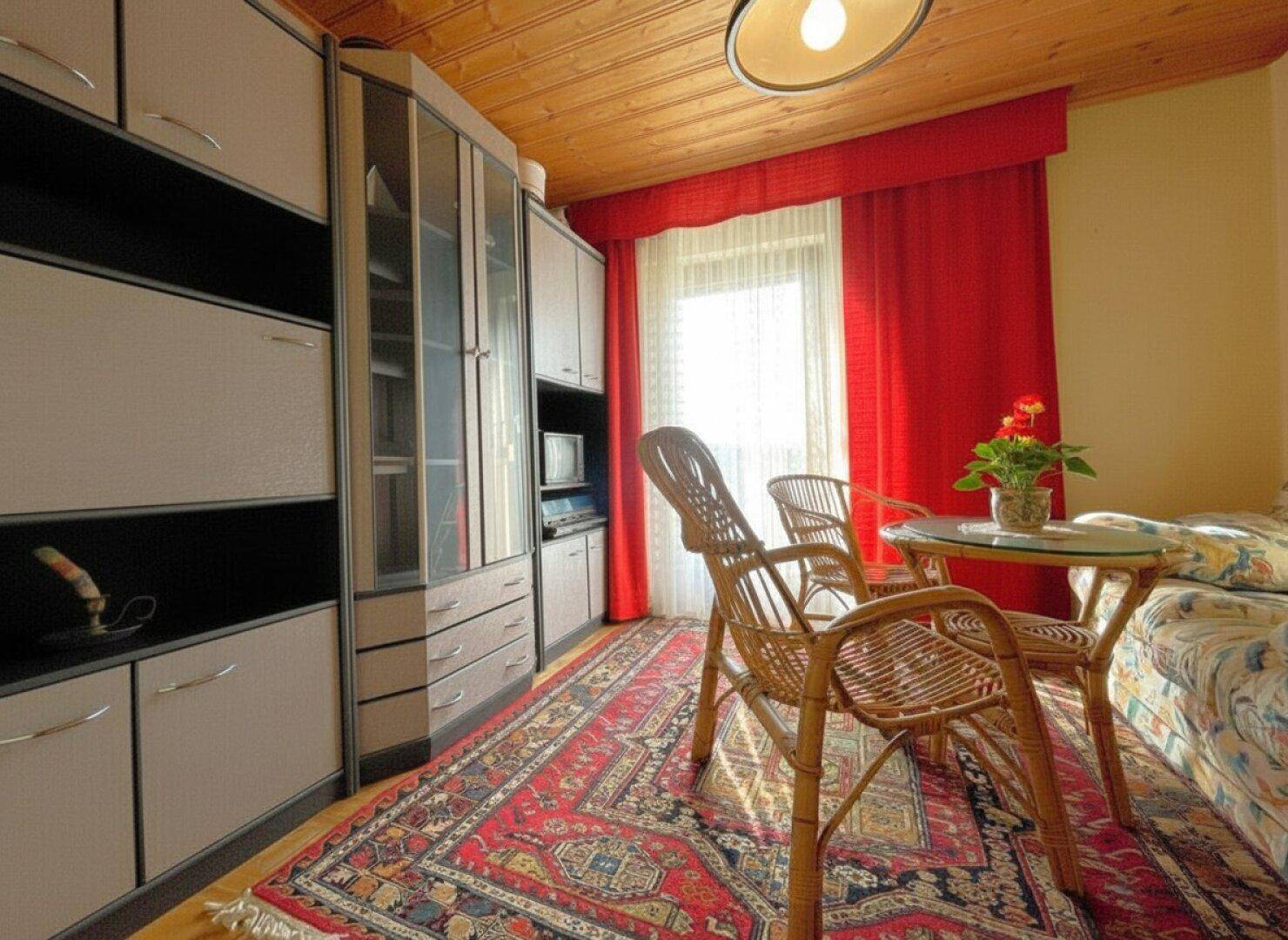 Gemütliches Zimmer mit Holzdecke, Einbauschränken und einem kleinen Sitzbereich am Fenster.