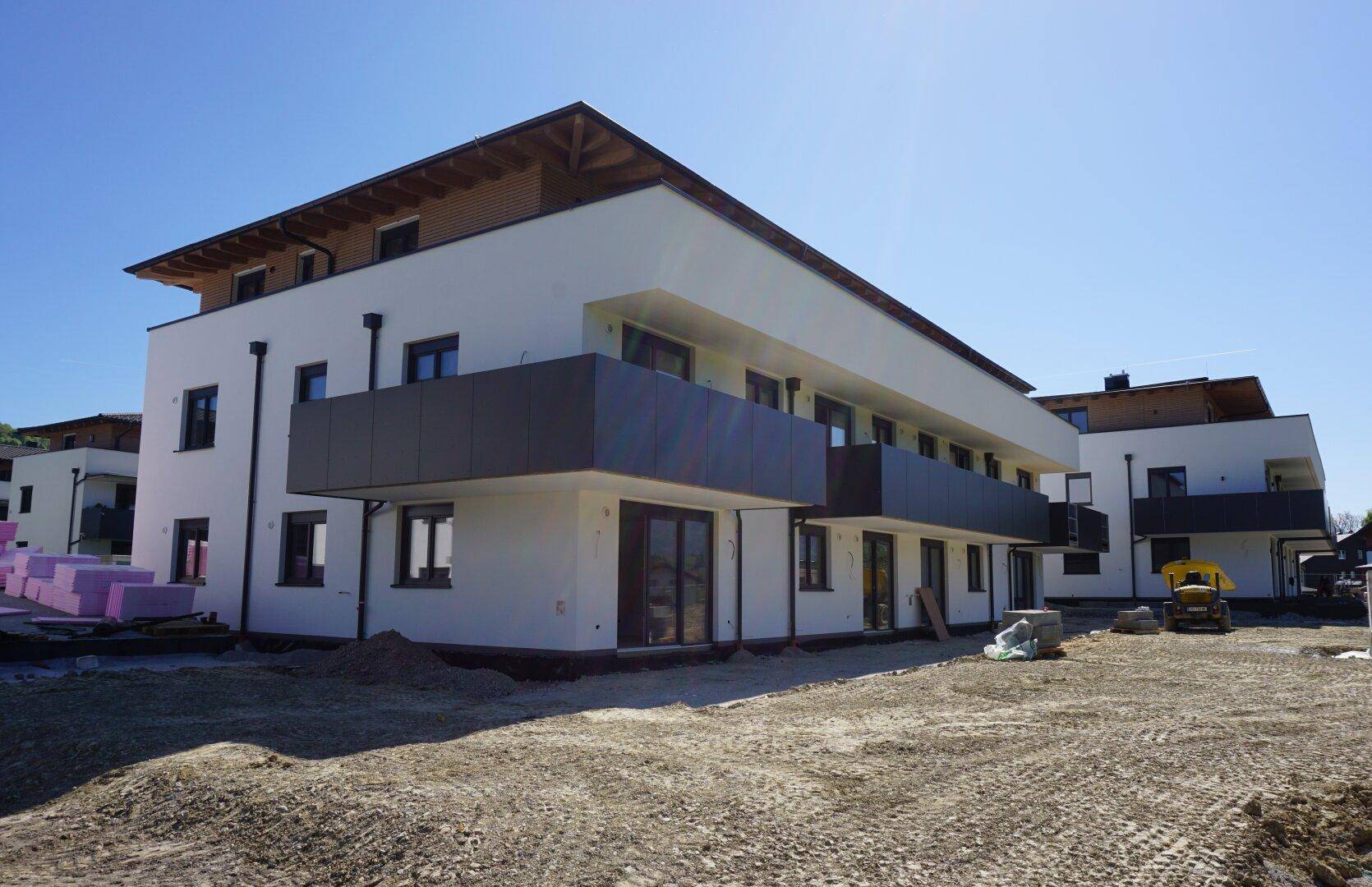 Moderne Neubauwohnungen mit Balkonen und großen Fensterfronten, umgeben von einer Baustelle mit Bergblick.