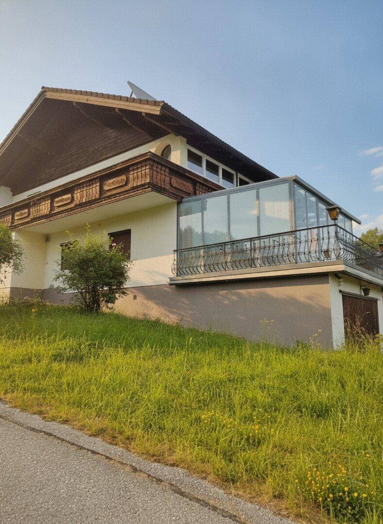 Detailansicht des Hauses mit dem verglasten Wintergarten und dem verzierten Holzbalkon.