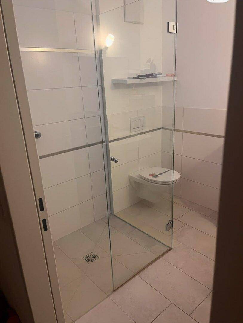 Modernes Badezimmer mit weiß gefliesten Wänden, begehbarer Dusche und wandhängendem WC.