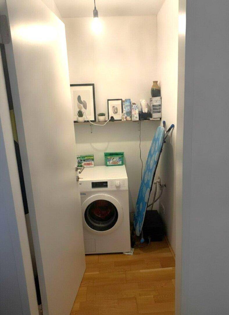 Praktischer Hauswirtschaftsraum mit Waschmaschine, Bügelbrett und Regalen für Vorräte.