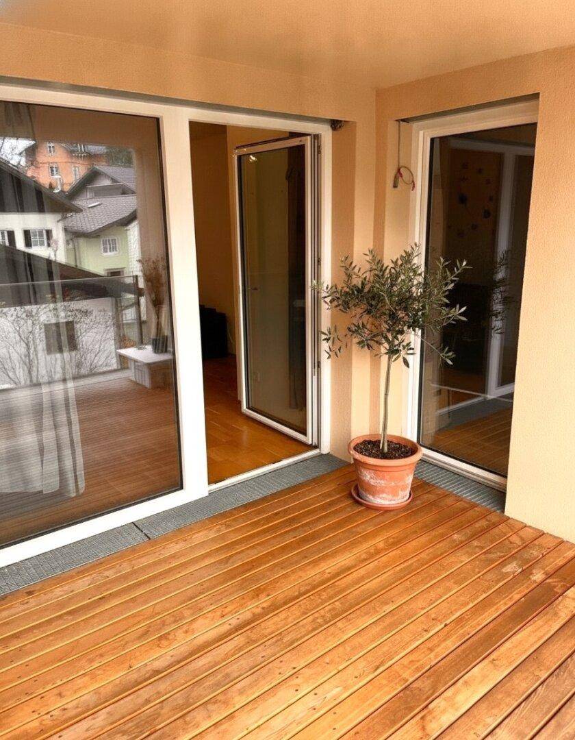 Heller Balkon mit Holzfußboden, Glasgeländer und einer Topfpflanze.