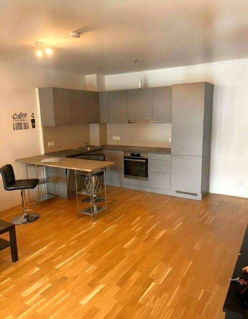 Moderne Küche mit grauen Schränken, Holzboden und einer integrierten Essecke.