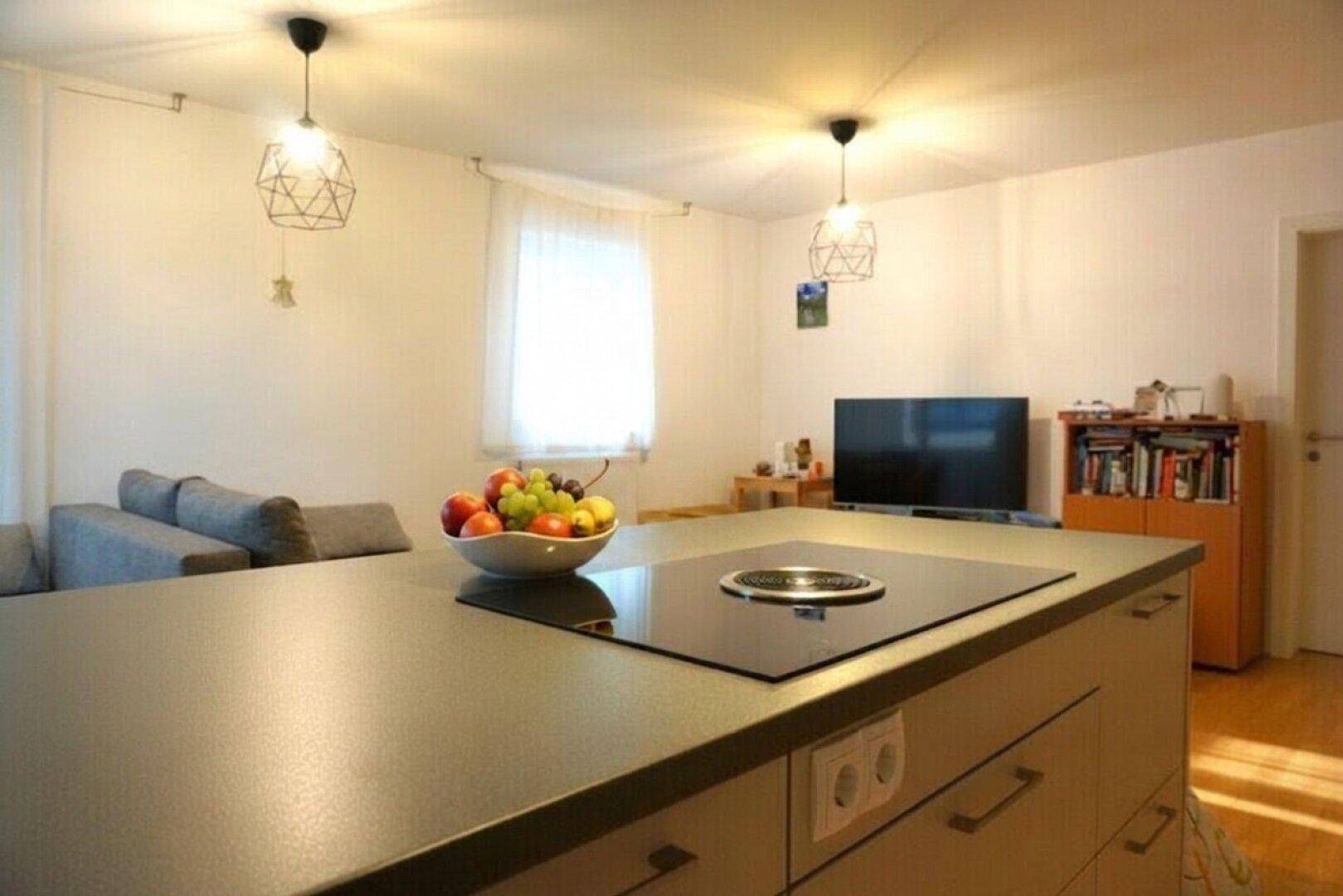 Kücheninsel mit Induktionskochfeld im offenen Wohnbereich, ergänzt durch Sofa und Bücherregal.