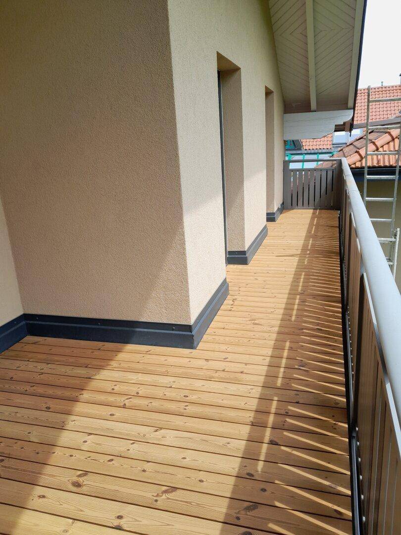 Langer Balkon mit Holzdielenboden und Blick auf die Umgebung, gut beleuchtet.