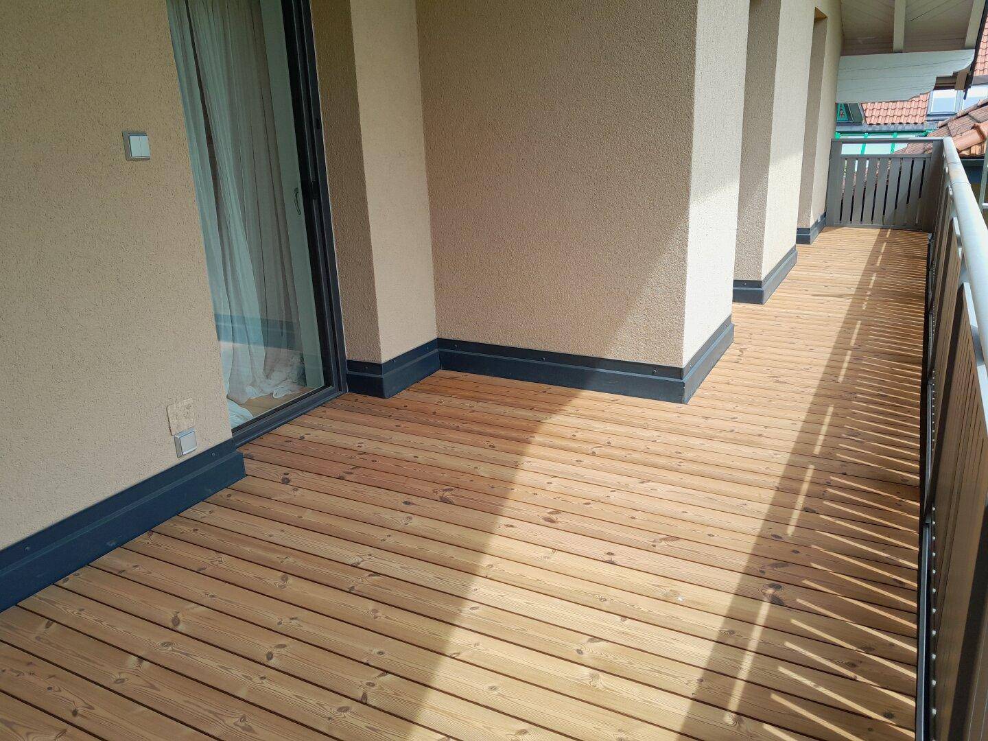 Langer Holzbalkon mit Metallgeländer, ideal für sonnige Stunden und weitem Blick.