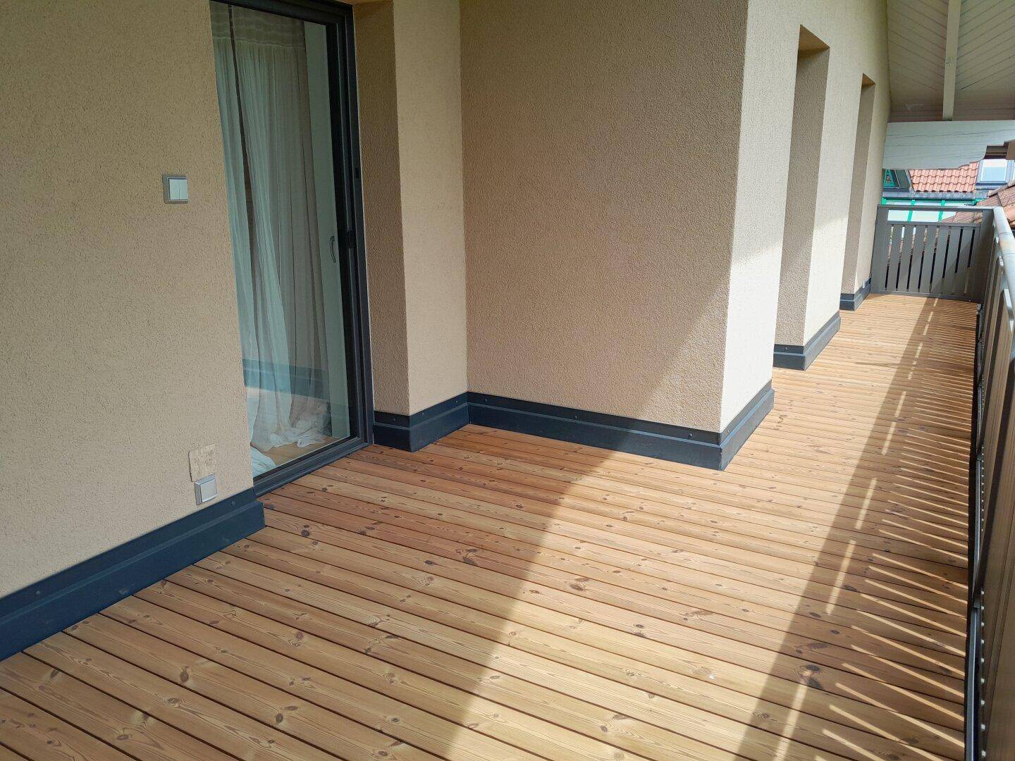 Heller Balkon mit Holzdielenboden und Zugang durch eine große Glasschiebetür.