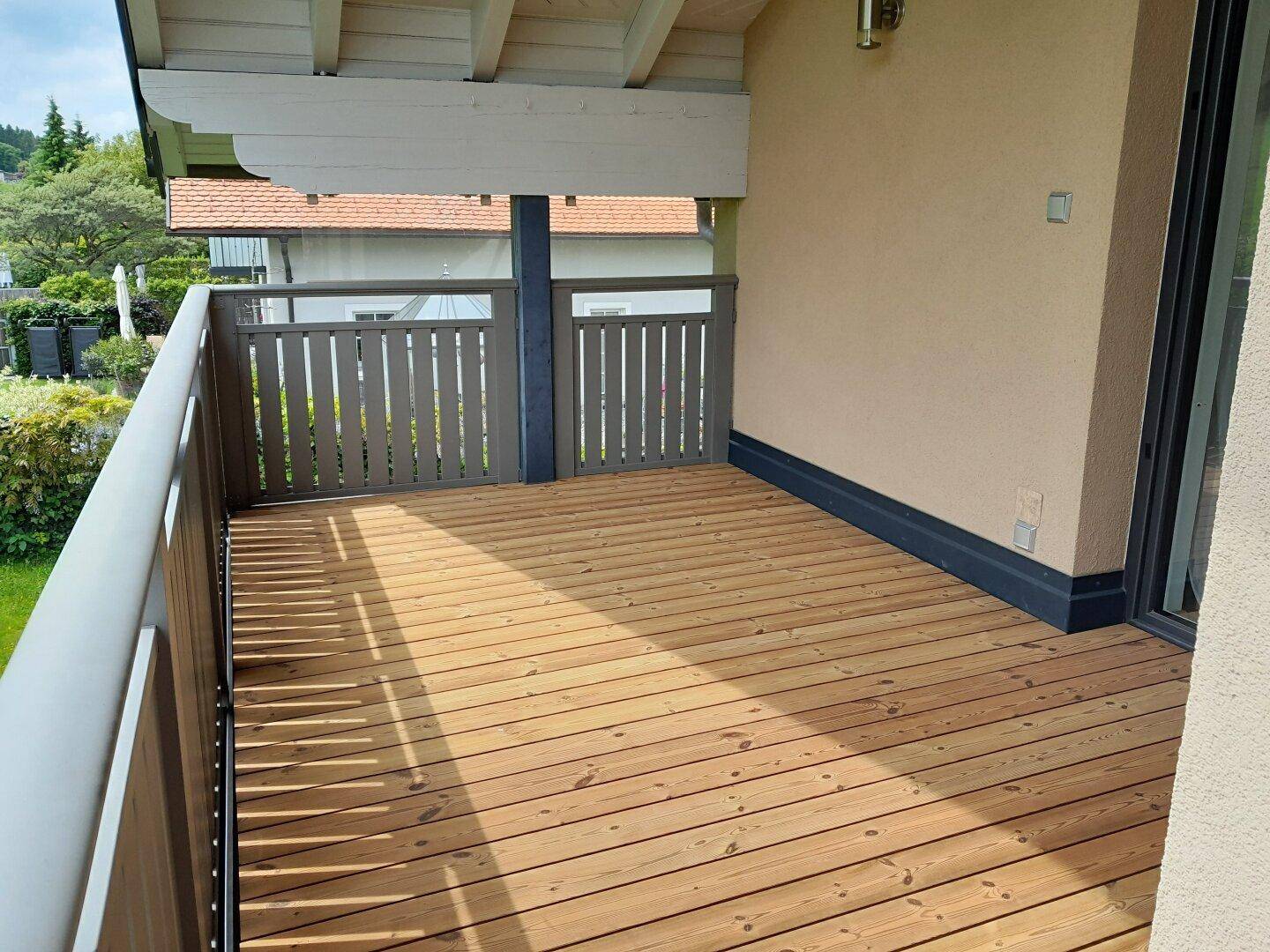 Geräumiger Holzbalkon mit modernem Geländer und sonnigem Ausblick in die Natur.