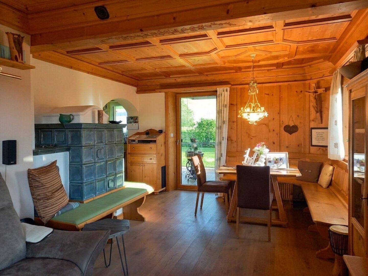 Rustikaler Wohn- und Essbereich im alpinen Stil mit Holztäfelung, Kachelofen und Gartenzugang.